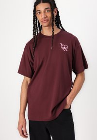 Mørkerød bomulds t-shirt med korte ærmer og løs pasform, med et pink hjerte grafik med en pil på venstre bryst.