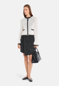 White crochet cardigan with black trim, paired with a black pinstripe skirt. Black handbag and polka dot flats complete the outfit.