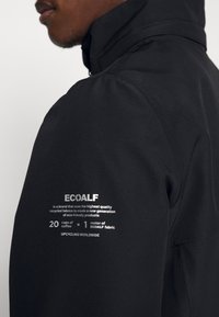 Černá bunda ECOALF s vysokým límcem, texturovanou tkaninou a bílým potiskem, který označuje ekologický původ a metodu výroby materiálu.