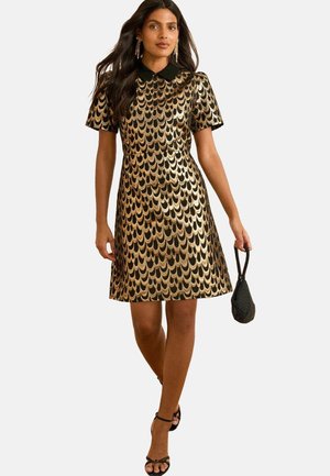 Gold- und schwarz gestreifter Kleid mit kurzen Ärmeln und einem schwarzen Kragen. Kombiniert mit einer kleinen schwarzen Tasche und schwarzen Sandalen mit Riemchen.