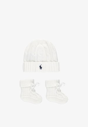 Cappellino bianco per neonati lavorato a maglia con un piccolo logo nero e scarpine abbinate con lacci, entrambe caratterizzate da motivi a trecce.