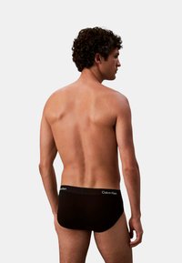 Schwarze Baumwoll-Slips mit einem Taillenbund mit Logo, die eine eng anliegende Passform und eine glatte Textur aufweisen. Das Design ist minimalistisch und funktional.