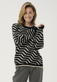 Black and white zigzag pattern sweater with a round neckline and long sleeves. Textured fabric and contrasting trim details at cuffs and hem.