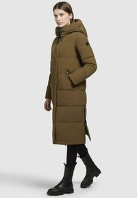 Long olive green puffer coat with a hood, featuring zippered pockets and ribbed cuffs. Smooth texture with visible quilted pattern.