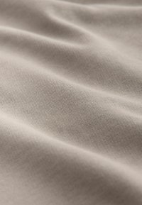 Jasnobeżowa tkanina o gładkiej fakturze, ukazująca miękkie fałdy i subtelne rozciągnięcie, głównie wykonana z bawełny lub podobnego materiału.