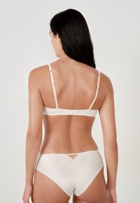 Reggiseno beige e slip abbinati con una superficie liscia di satin. Il reggiseno presenta spalline regolabili e chiusura con gancio; il slip ha un piccolo dettaglio a taglio.