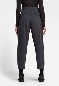 Mörkgrå arbetsbyxor med avslappnad passform, som har fickor med överlägg, stickade detaljer och uppvikta fållar. Materialet verkar hållbart med en lätt lyster.