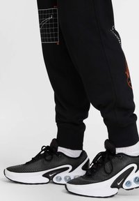 Pantalones de chándal negros con estampado gráfico y puños elásticos, combinados con zapatillas Nike en blanco y negro con parte superior de malla y amortiguación de aire.