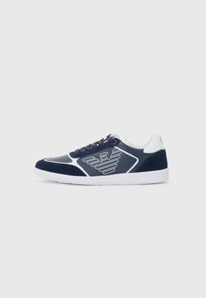 Navy blue sneakers with white accents, featuring textured fabric, smooth panels, perforations, and logo detailing on the sides.