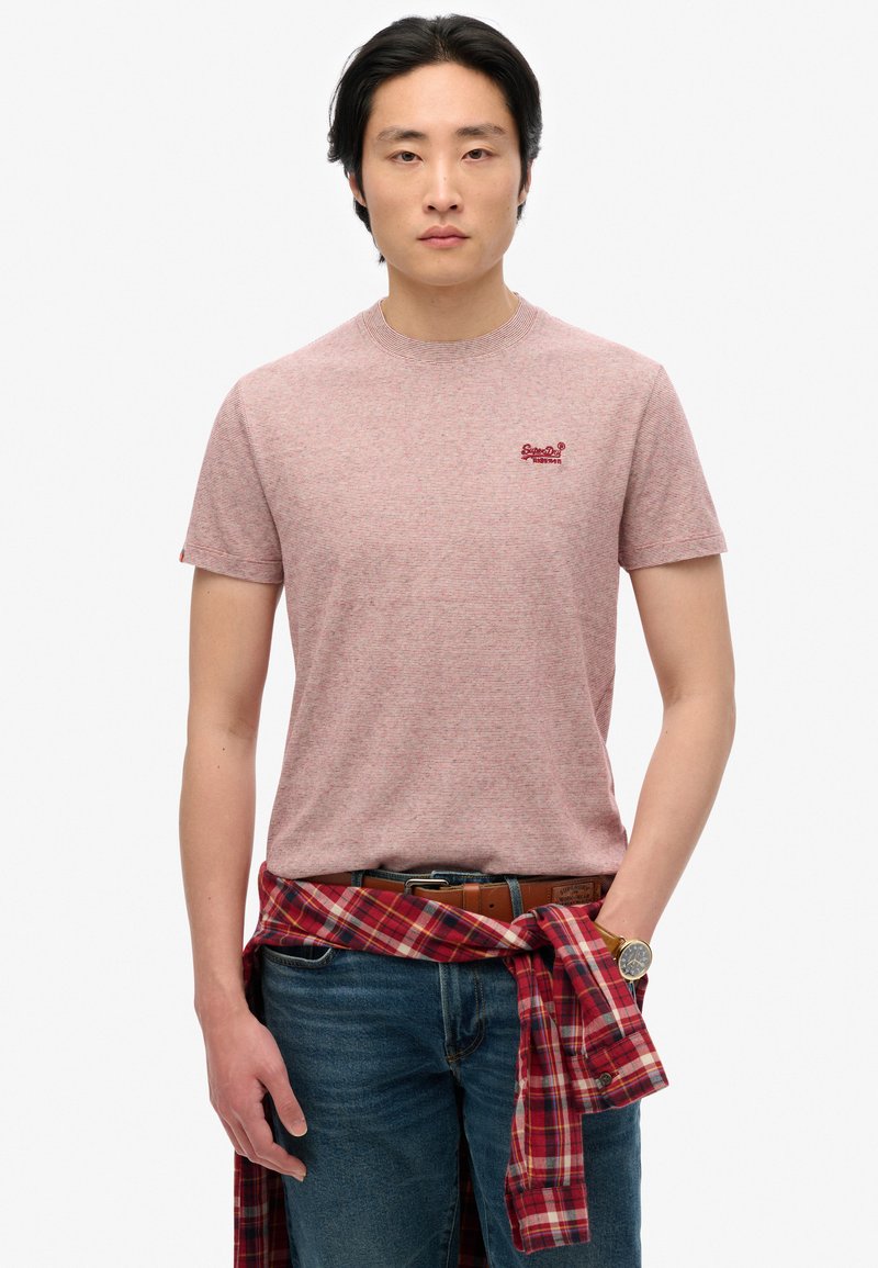 Camiseta de manga corta a rayas rojas y blancas con cuello redondo, combinada con jeans azules. Una camisa de franela a cuadros rojos está atada a la cintura.