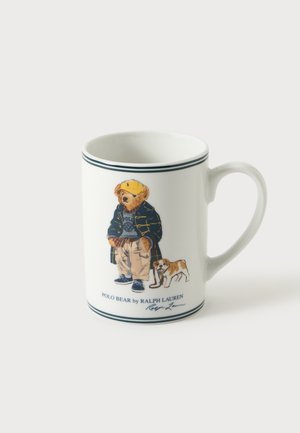 Tasse blanche avec illustration d’un ours portant des vêtements décontractés et une casquette, debout avec un petit chien, texte Polo Bear par Ralph Lauren en dessous.