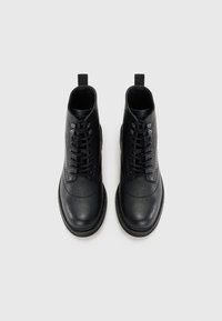 Botas de tobillo negras de cuero texturizado, con un diseño de cordones, punta redondeada y una lengüeta, que presentan un acabado liso a lo largo de los bordes.