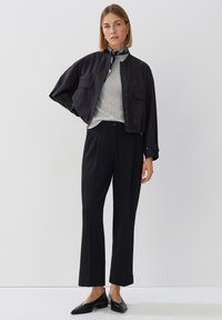 Zwarte cropped jasje over een lichtgrijze textuur top, gecombineerd met zwarte wijde broek en zwarte platte schoenen, inclusief een gestreepte sjaal.