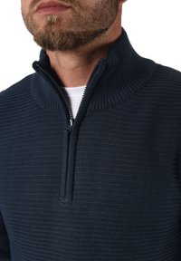 Pull en maille bleu marine avec un col haut et une fermeture éclair demi-longueur. Tissu texturé et couleur unie, avec une doublure intérieure lisse.