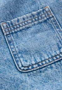 Denim-tasku vaaleansinisessä sävyssä, jossa on näkyvät ompeleet. Pintatekstuurissa on hieman kuluneen näköistä ja se on sileä. Tasku on neliönmuotoinen eikä siinä ole kuvioita.