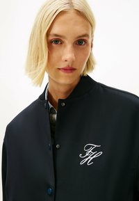 Marine bomberjack gemaakt van gladde stof, met een ribbelkraag, drukknoopsluiting en witte geborduurde initialen op de borst.