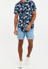 Chemise à manches courtes bleu marine à motif floral blanc, associée à un short en jean retroussé et des baskets blanches. Tenue décontractée d'été.