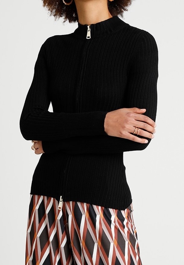 Pull zippé noir à côtes, avec un col haut et une coupe ajustée. Doté d'une fermeture éclair argentée et de manches longues. Associé à un pantalon à motifs.