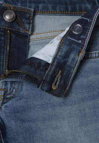 Jeans de mezclilla azul con cremallera, que presentan costuras amarillas contrastantes y herrajes de latón. El interior muestra un forro suave.