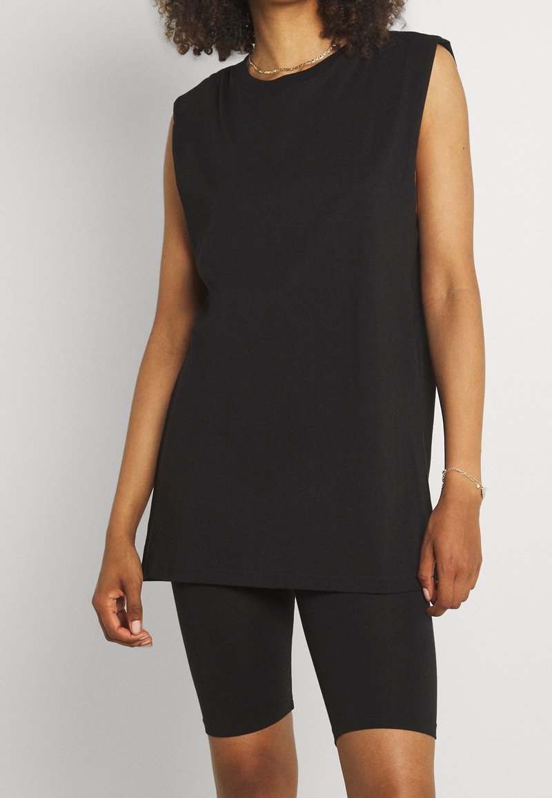 Haut noir sans manches en coton, avec une coupe décontractée et un col rond, assorti à des shorts de cycliste noirs. Texture lisse, design minimaliste.