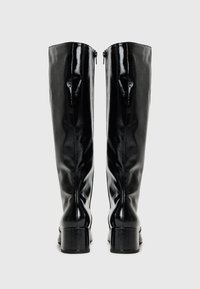 Botas pretas até ao joelho feitas de um couro sintético brilhante. Possuem um salto quadrado e um fecho com zip na parte de trás. Textura lisa e design ajustado.