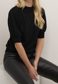 Sort kortærmet sweater i blød, struktureret strik med høj hals og puffede ærmer, matchet med sorte tætsiddende læderbukser.