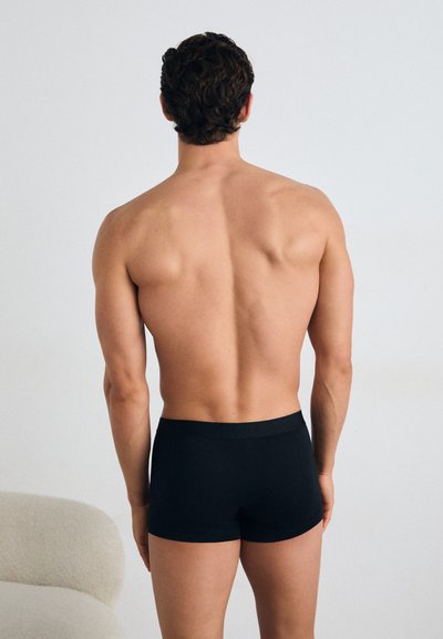 Boxer-briefs pour hommes noirs en tissu doux. Taille basse, design ajusté, sans motifs visibles. Modèle vu de dos.