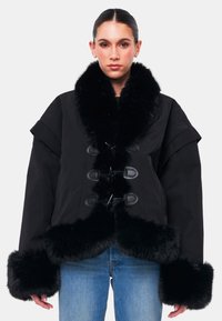 Giacca nera oversize con colletto e polsini in pelliccia sintetica, dotata di chiusure a bottone e tessuto texture. Design durevole e caldo.