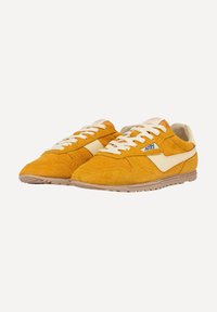 Sneakers in suede giallo senape con accenti crema. Presentano una chiusura a lacci classica e una suola in gomma con un brandizzamento sottile sul lato.