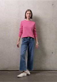Maglione rosa a maglia, vestibilità rilassata, maniche a tre quarti. Jeans azzurri a gamba larga, risvolti all'orlo. Sneakers bianche, calzature informali.