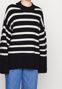 Black and cream striped knit sweater with a wide ribbed design and a relaxed fit. Features a round neckline and oversized sleeves.