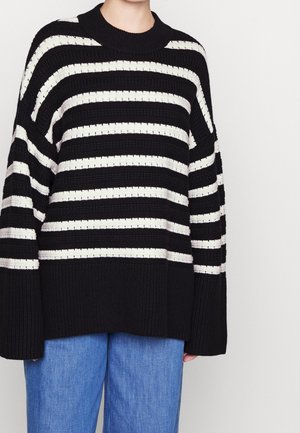 Maglione a righe nero e crema con un ampio design a coste e una vestibilità rilassata. Presenta un collo rotondo e maniche oversize.