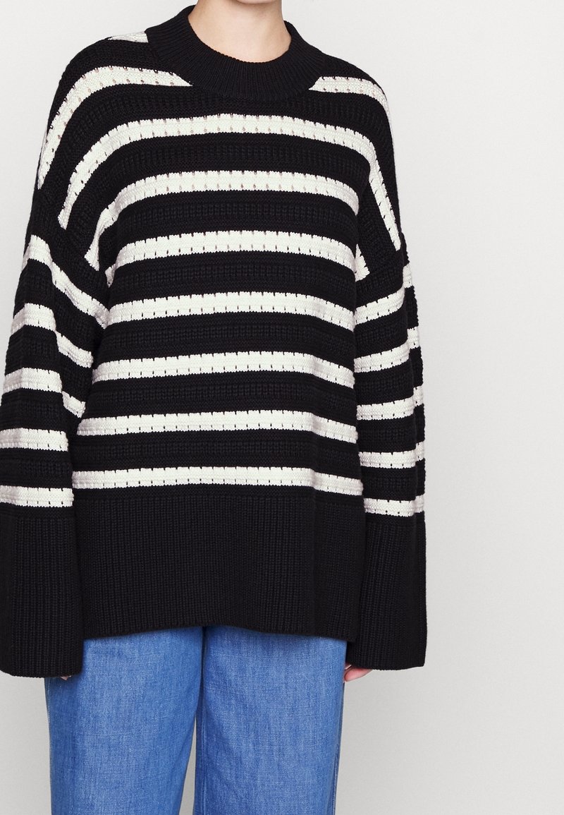 Black and cream striped knit sweater with a wide ribbed design and a relaxed fit. Features a round neckline and oversized sleeves.