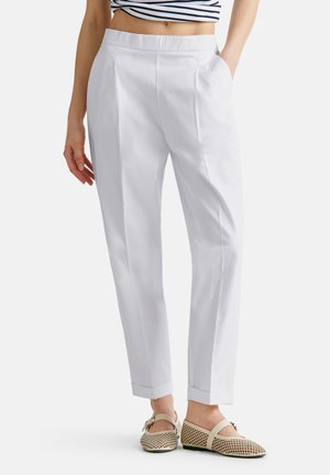 Los pantalones blancos ajustados presentan un frente plano con pliegues, bolsillos laterales y dobladillos con vuelta, combinados con unas bailarinas de malla de color claro.
