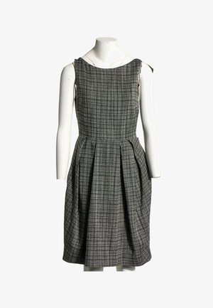Robe sans manches longueur genoux avec motif à carreaux noir et blanc, corsage ajusté et jupe plissée, présentée sur un mannequin blanc.