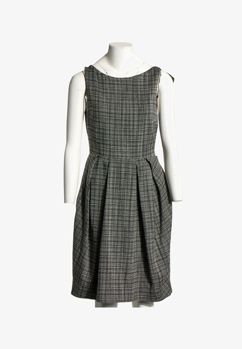 Robe sans manches longueur genoux avec motif à carreaux noir et blanc, corsage ajusté et jupe plissée, présentée sur un mannequin blanc.