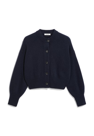 Modra kratka jopica iz mehkega pletenega blaga. Ima okroglo izreznico, dolge rokave in šest črnih gumbov spredaj.