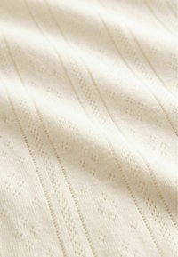 Textured cream fabric featuring vertical lines and small diamond patterns, with a soft, knitted appearance and subtle weave details.