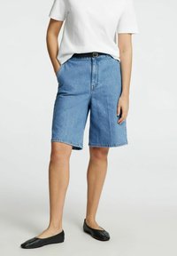 Jeansshorts i ljusblått, med rak passform, sidofickor och en lätt fransad nederkant. Bärs med ett svart bälte och svarta ballerinas.