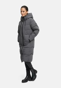 Gray puffer coat with zip closure, hood, and side pockets. Features quilted design and embroidered logo on sleeve. Paired with black boots.