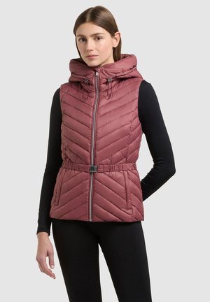 Kobieta w miękkiej fioletowej pikowanej kamizelce bez rękawów z kapturem, z zamkiem błyskawicznym z przodu i paskiem w talii, nosząca pod nią czarną bluzkę z długim rękawem i spodnie.