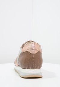 Tenisky s kovově růžovým zlatem a texturovanou hnědou kůží, s bílou podrážkou a hladkými akcenty. Zadní pohled ukazuje designové detaily.