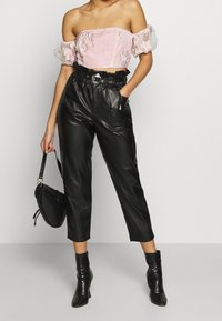Crop top rose à épaules dénudées avec broderies florales, associé à un pantalon taille haute en similicuir noir et des bottines noires. Sac noir inclus.