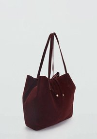 Burgundy mockaskväska med två långa remmar, slät yta, platt botten och fyrkantiga metallackenter i närheten av öppningen.