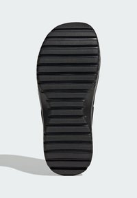 Sort sneakersål med tykk, struktureret gummi, der har vandrette og lodrette riller til greb. Glat kant og rund tådesign.