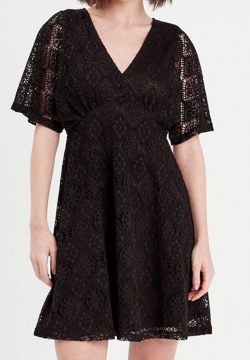 Robe en dentelle noire avec un col en V, des manches courtes et une jupe évasée. Présente des motifs floraux complexes et une taille cintrée.