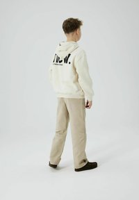 Felpa color crema con testo nero sul retro, abbinata a pantaloni beige e scarpe scure. Design semplice e texture morbida, adatta per un abbigliamento casual.