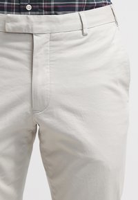 Beige bomullsbyxor med slät textur, med platt framstycke, sidfickor och bälteshällor, visade tillsammans med en rutig skjorta.