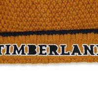 Bonnet orange tricoté avec un motif texturé et une bande noire arborant "TIMBERLAND" en lettres blanches en gras.