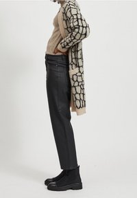 Beige mönstrad cardigan, brun topp, svarta läderbyxor och svarta ankelstövlar. Cardigan har en rutmönstring, mjuk textur och lång längd.